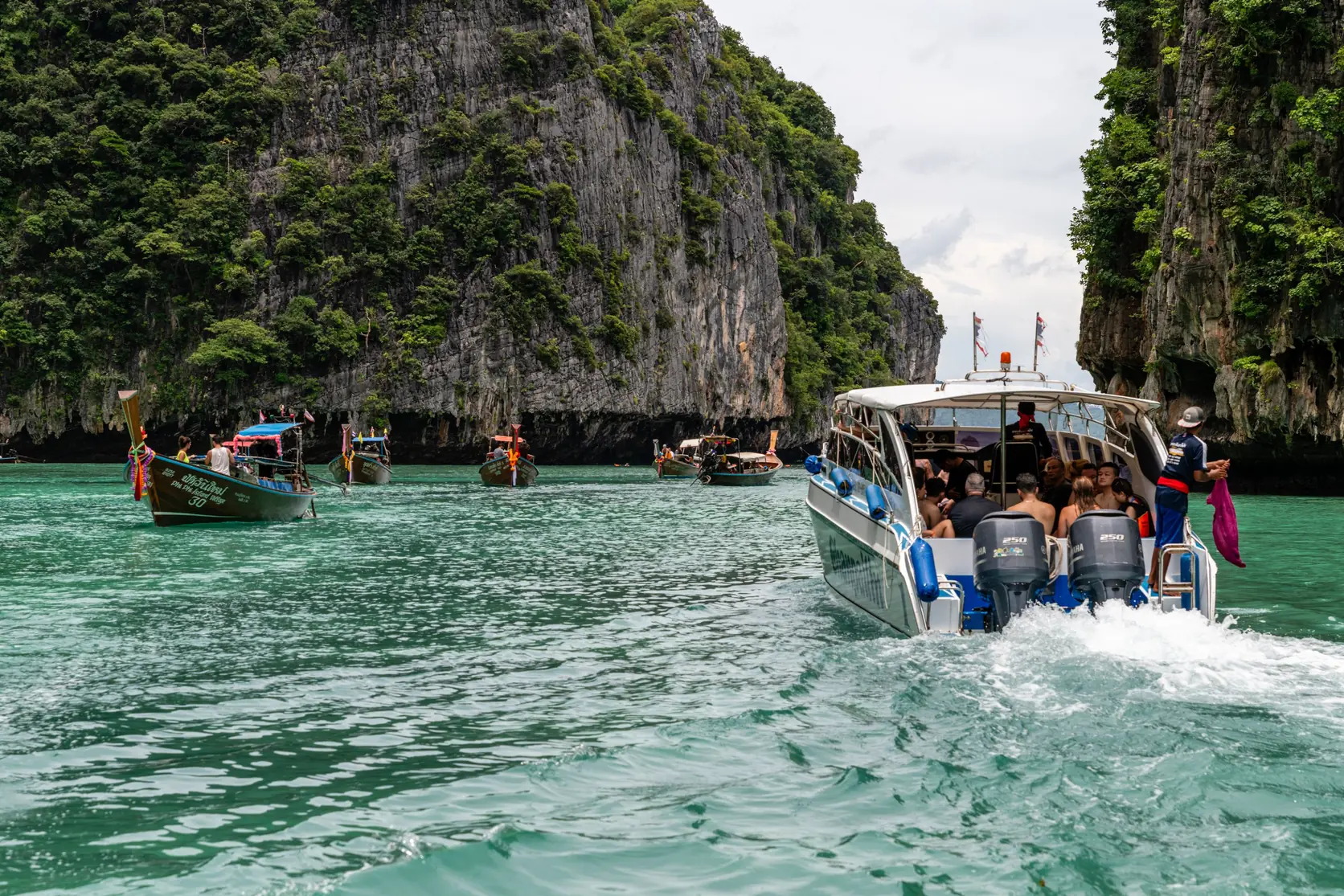 A speedboat and longtail boats between limestone cliffs