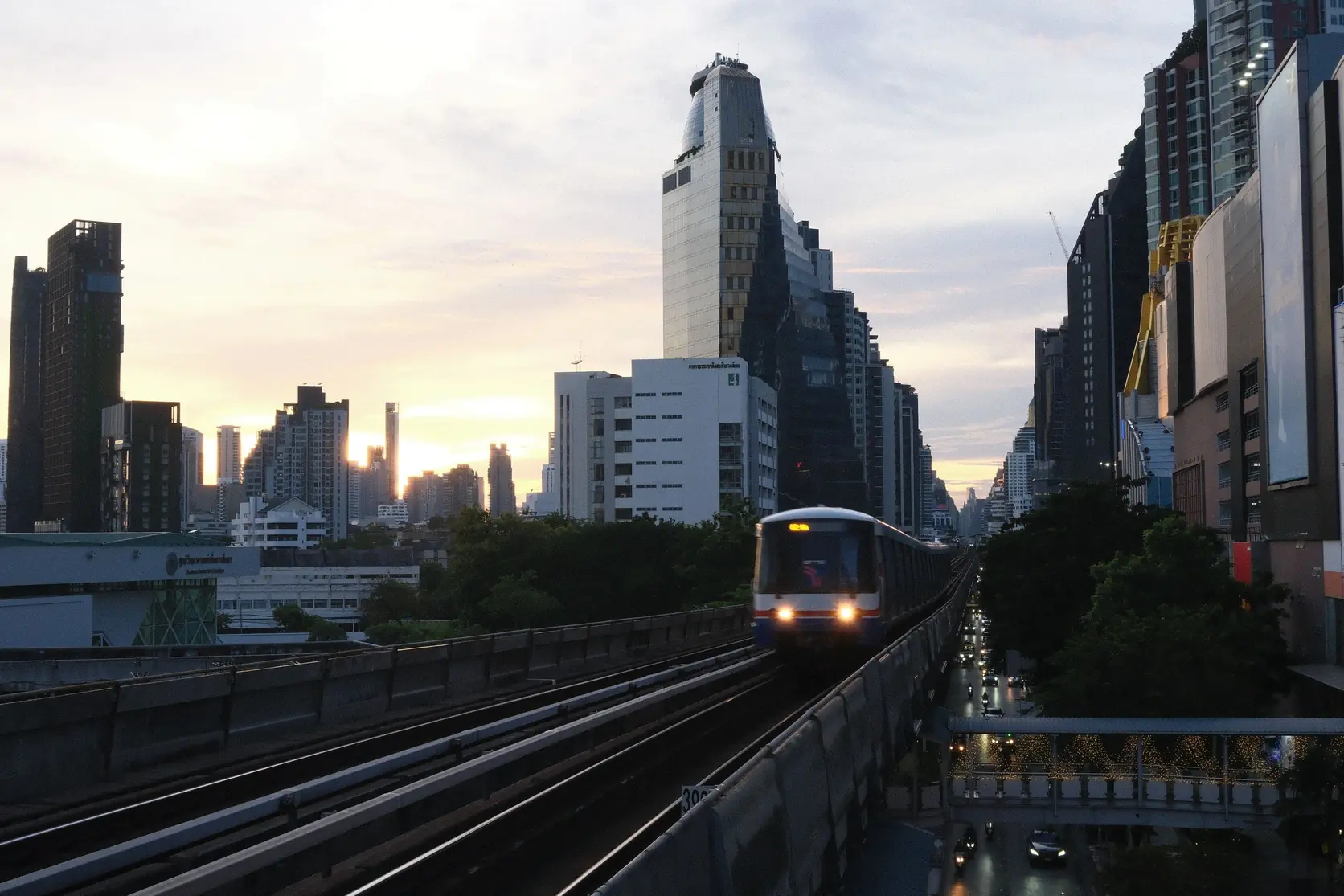 Ein BTS-Skytrain auf der Hochbahn vor Bangkoks Skyline in der Dämmerung
