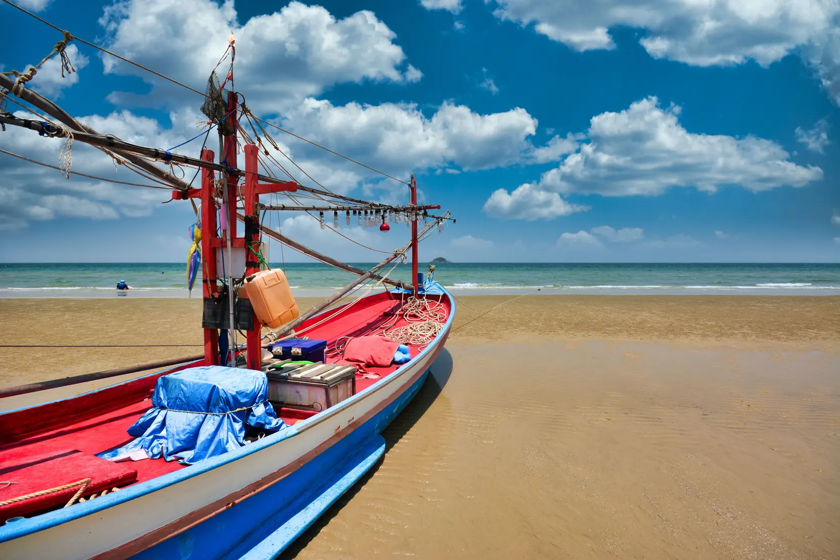 A red and blue fishing boat on the sand of Hua Hin beach