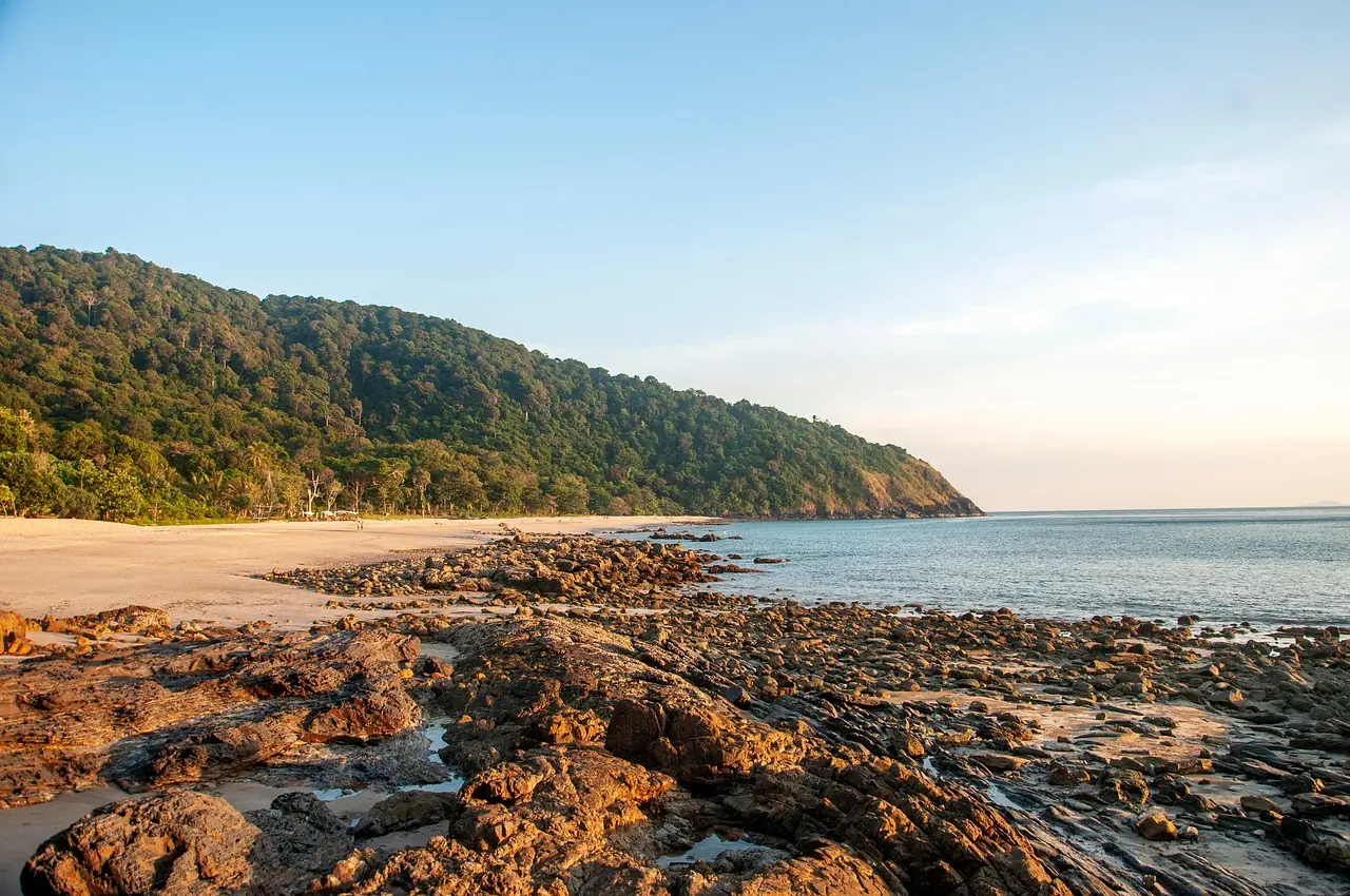 Una playa tranquila y rocas planas bajo un cabo boscoso en Koh Lanta